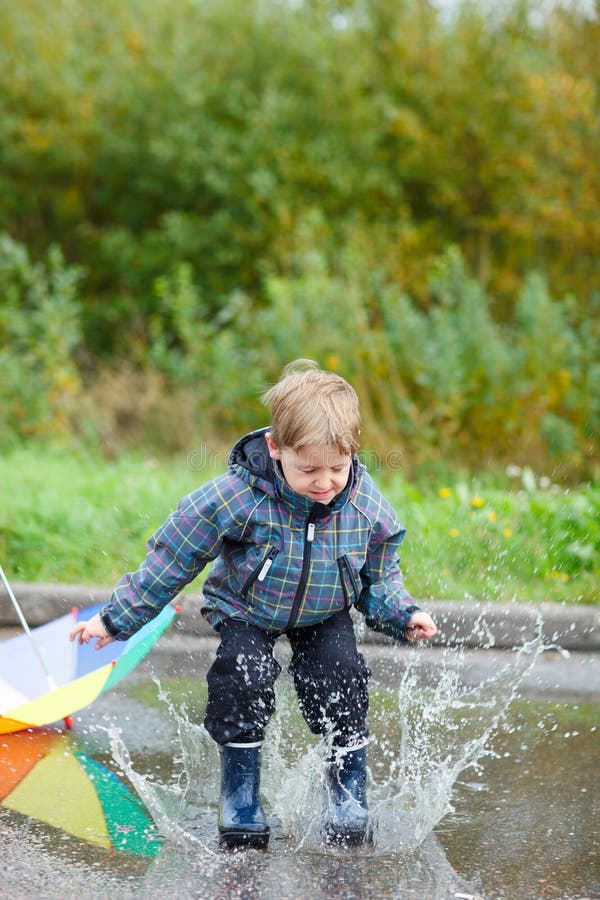 Playful boy jumping in puddle on rainy autumn day