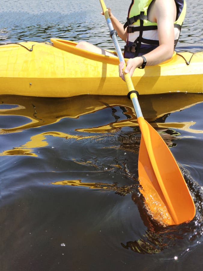 A Boy in a Kayak in a Life Jacket Pulls Out an Oar. Side View. Active