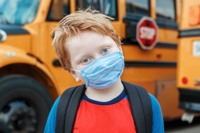 Boy kid student in protective face mask near school yellow bus outdoor. New normal at coronavirus covid-19 pandemic. Measurements stock photo Boy kid student in protective face mask near school yellow bus outdoor. New normal at coronavirus covid-19 pandemic. Measurements stock photo