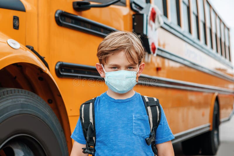 Boy kid student in protective face mask near school yellow bus outdoor. New normal at coronavirus covid-19 pandemic. Measurements stock image Boy kid student in protective face mask near school yellow bus outdoor. New normal at coronavirus covid-19 pandemic. Measurements stock image