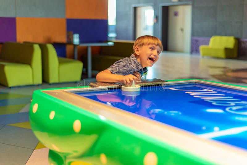 The boy laughs and rejoices in winning playing air hockey at the children`s entertainment center