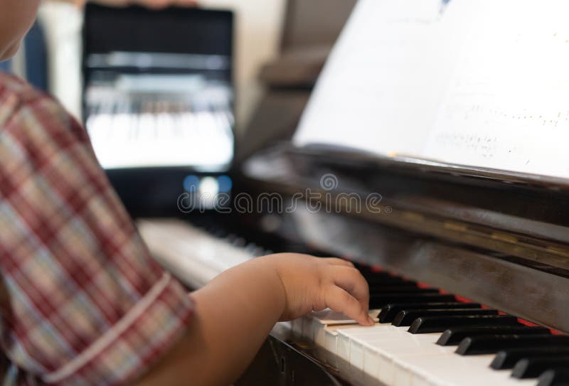 Foto de Young pianist boy looking at the digital tablet screen for learning piano  online at home. Music distance learning concept. do Stock