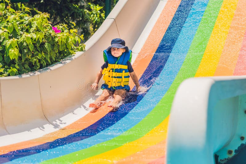 A Boy in a Life Jacket Slides Down from a Slide in a Water Park Stock