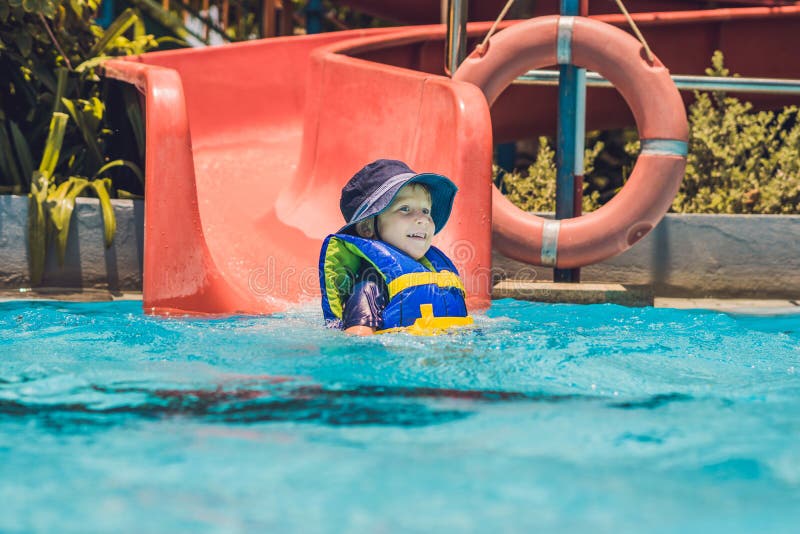 A Boy in a Life Jacket Slides Down from a Slide in a Water Park Stock