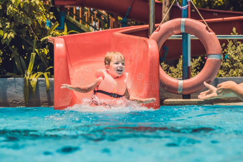 A Boy In A Life Jacket Slides Down From A Slide In A Water Park Stock