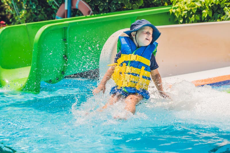 A Boy in a Life Jacket Slides Down from a Slide in a Water Park Stock