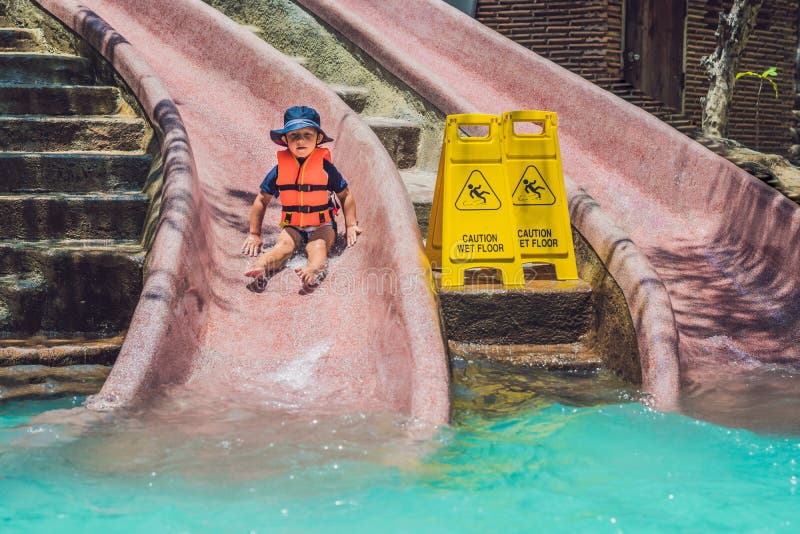A Boy in a Life Jacket Slides Down from a Slide in a Water Park Stock