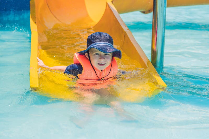 A Boy in a Life Jacket Slides Down from a Slide in a Water Park Stock