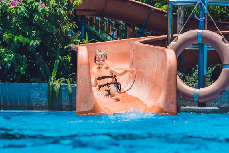 A Boy in a Life Jacket Slides Down from a Slide in a Water Park Stock