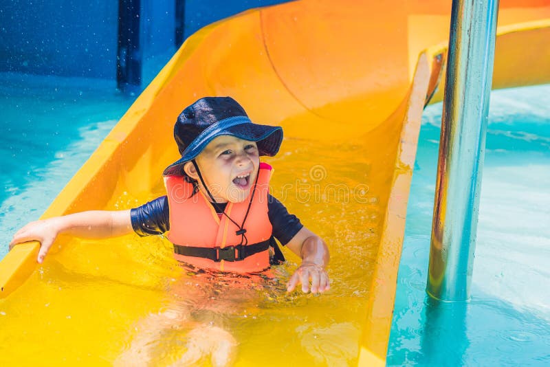 A Boy in a Life Jacket Slides Down from a Slide in a Water Park Stock