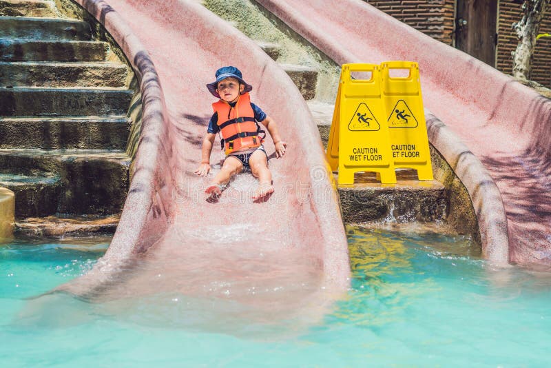 A Boy in a Life Jacket Slides Down from a Slide in a Water Park Stock