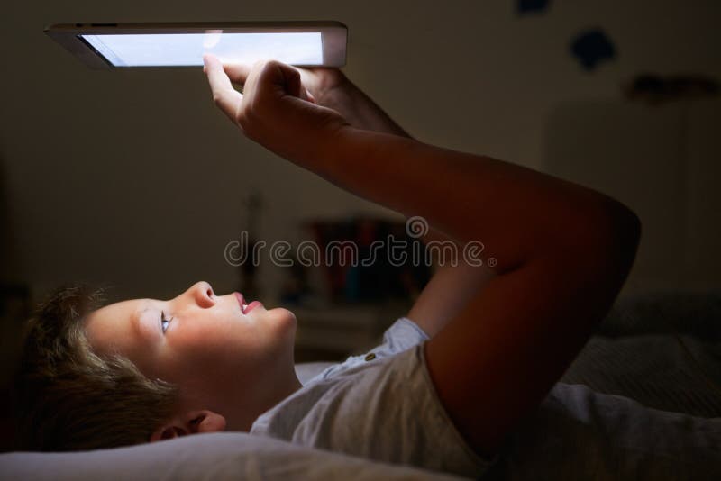 Boy Looking At Digital Tablet In Bed At Night