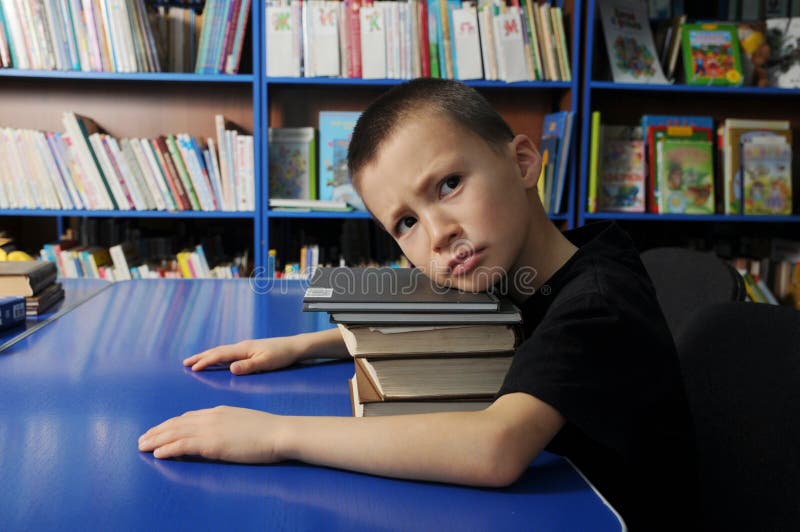 Boy looking groomy tired on pile of book in library don`t want to learning