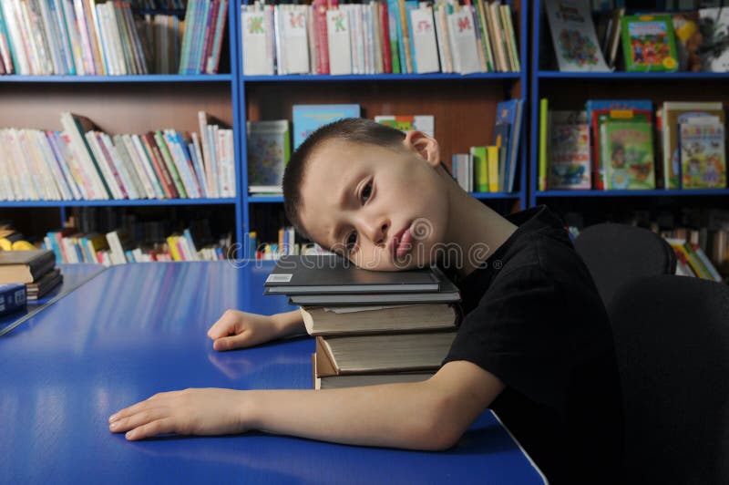 Boy lying tired on pile of book in library don`t want to learning