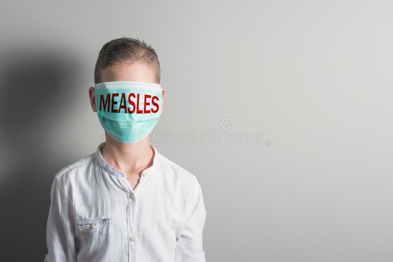 Boy in a medical mask with red inscription MEASLES on his face on bright background