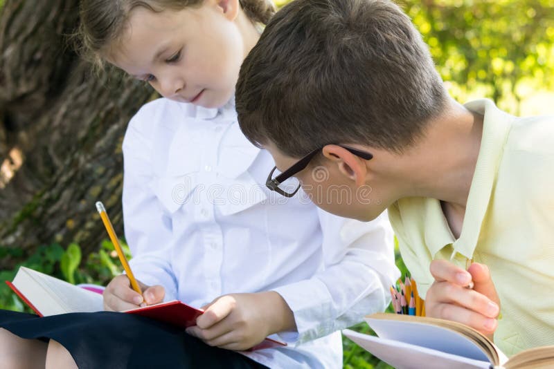 A boy peeps into a textbook for a girl during a lesson in a park, how to do a task from a teacher royalty free stock images A boy peeps into a textbook for a girl during a lesson in a park, how to do a task from a teacher royalty free stock images