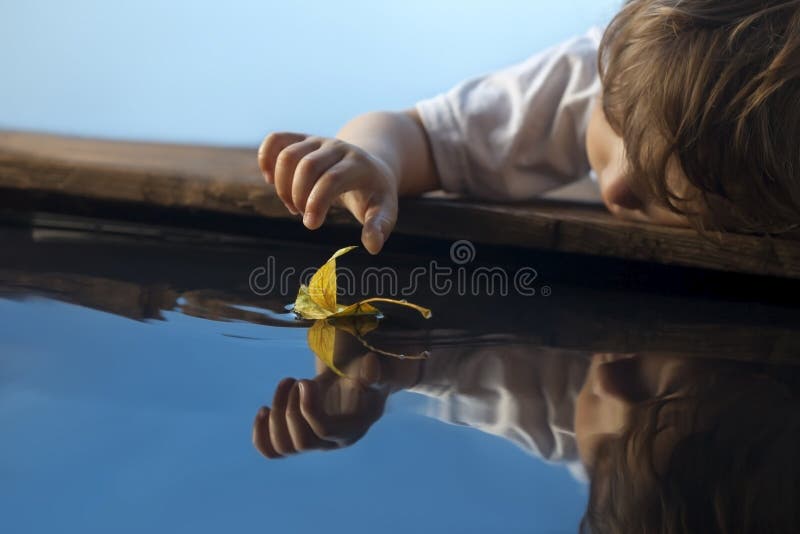 Boy play with autumn leaf ship in water, chidren in park play wi