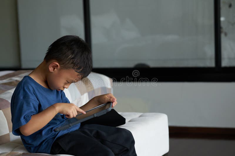 Boy play smart phone tablet in concentration alone in room in family care and ADHD concept