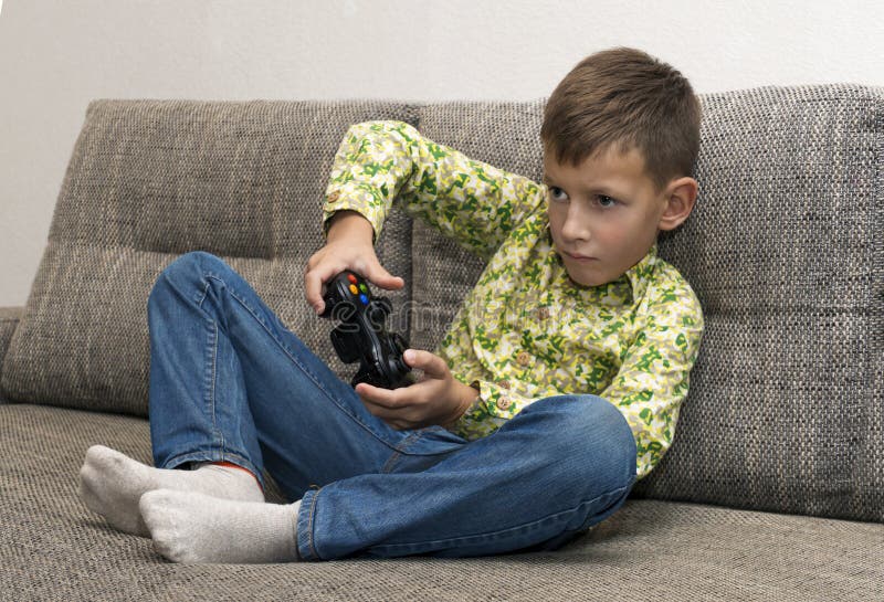 Boy playing video games with joystic sitting on sofa