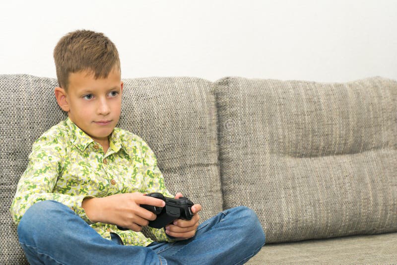 Boy playing video games with joystic sitting on sofa