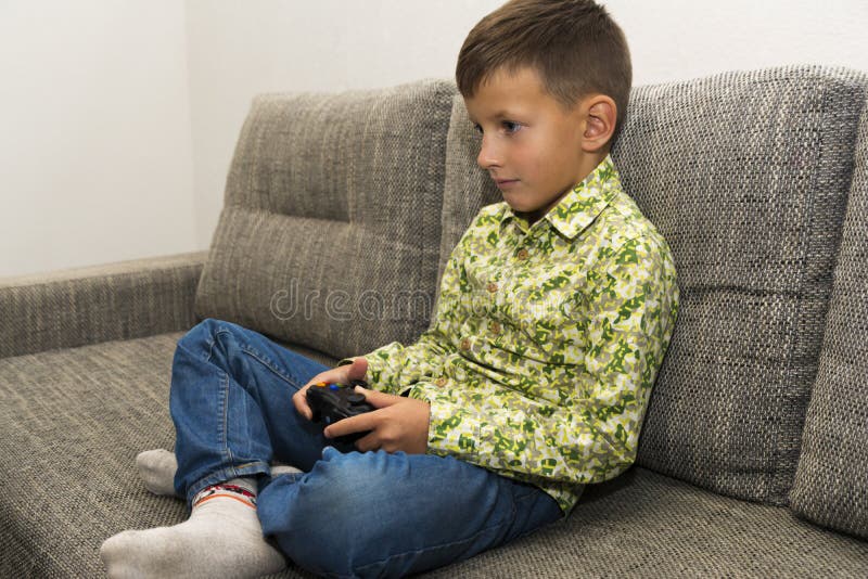 Boy playing video games with joystic sitting on sofa