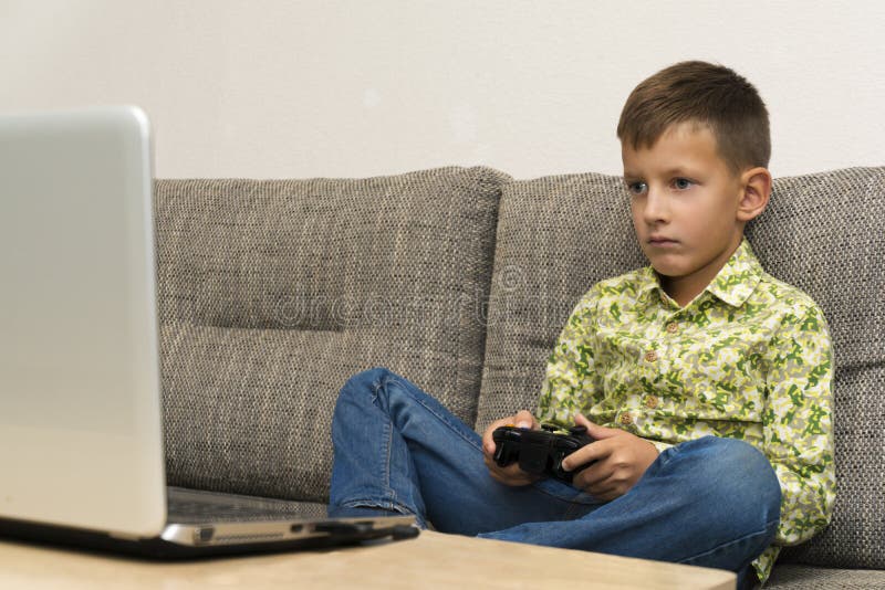 Boy playing video games with joystic sitting on sofa