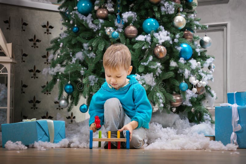 Boy playing with wooden hammer toy while sitting beside Christmas tree royalty free stock photography Boy playing with wooden hammer toy while sitting beside Christmas tree royalty free stock photography