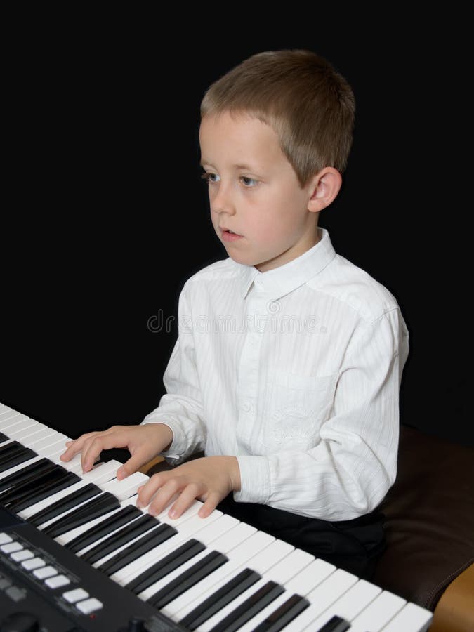 Boy plays keyborad, piano, looking in notes sheet