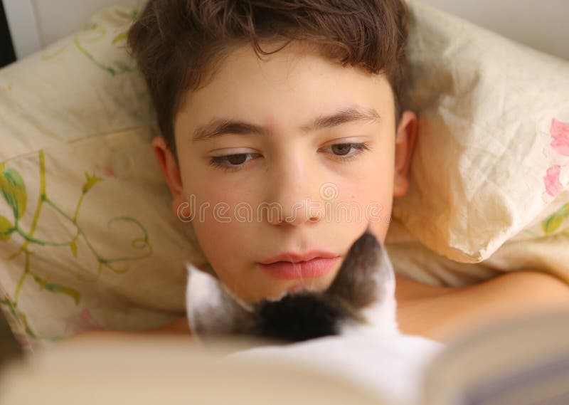 Boy reading book in bed with cat close up funny photo