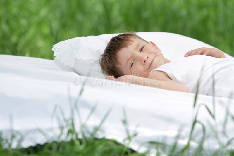 Boy relaxing on white bed on natural background