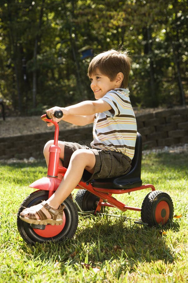 Side view of Hispanic boy riding red tricycle in grass. Side view of Hispanic boy riding red tricycle in grass.