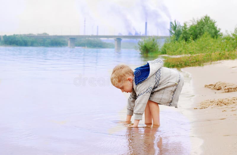 Boy on the river coast near plant