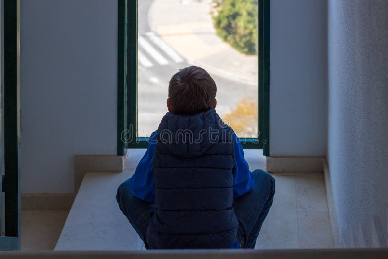 Sad boy sitting alone sitting in front of the window in the staircase