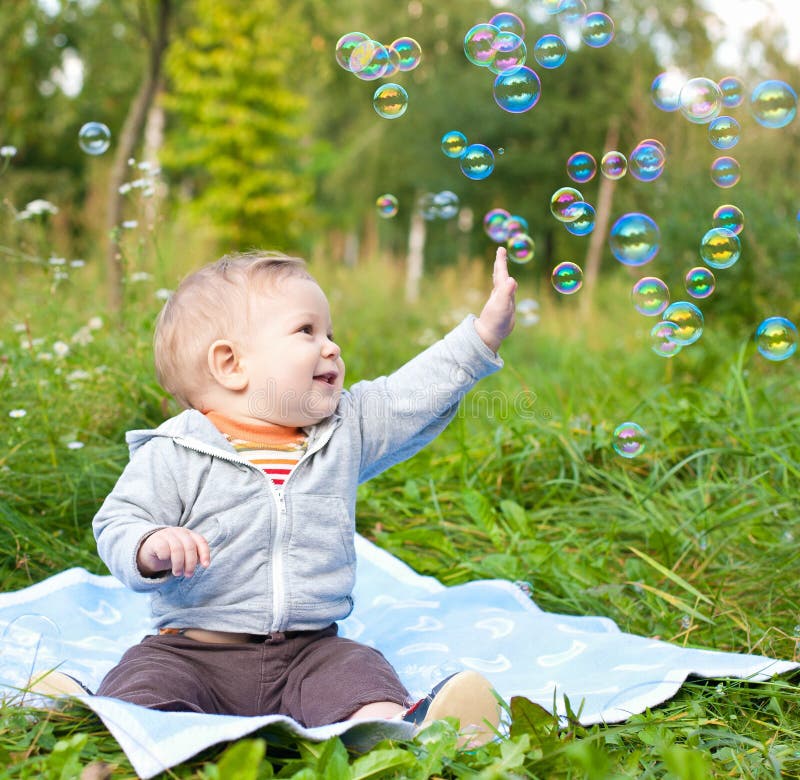 Bambino seduto sull'erba verde outdor a giocare con le bolle di sapone.