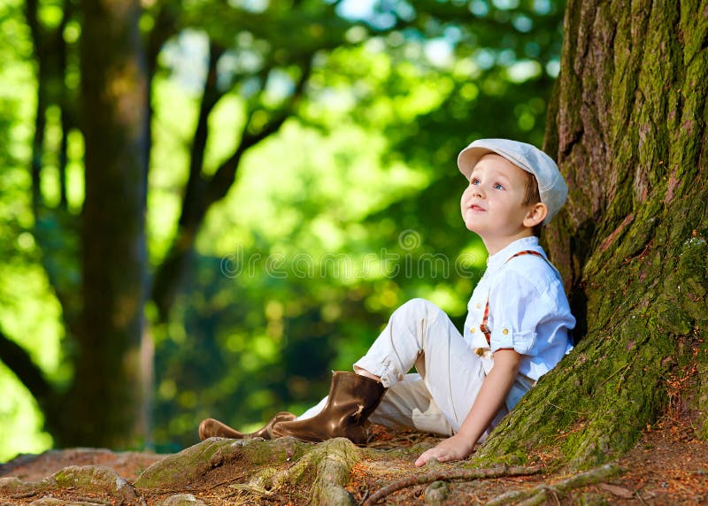 Cute boy sitting under an old tree, in the forest