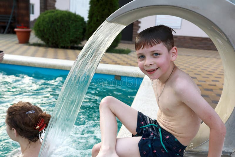 Boy sitting under stream of water in pool stock images