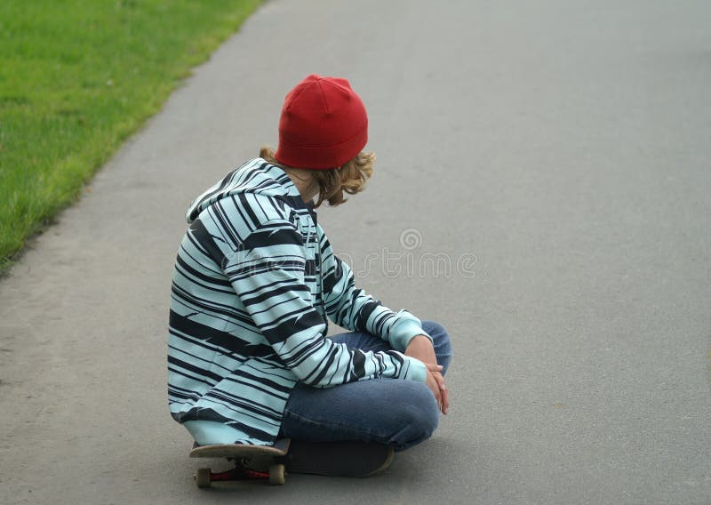 One boy, a teenager sitting on a skate board and look, boy dressed in a bright youth clothing on the head he wore a red cap on the street day. Bright red hat stock images, royalty-free photos and pictures