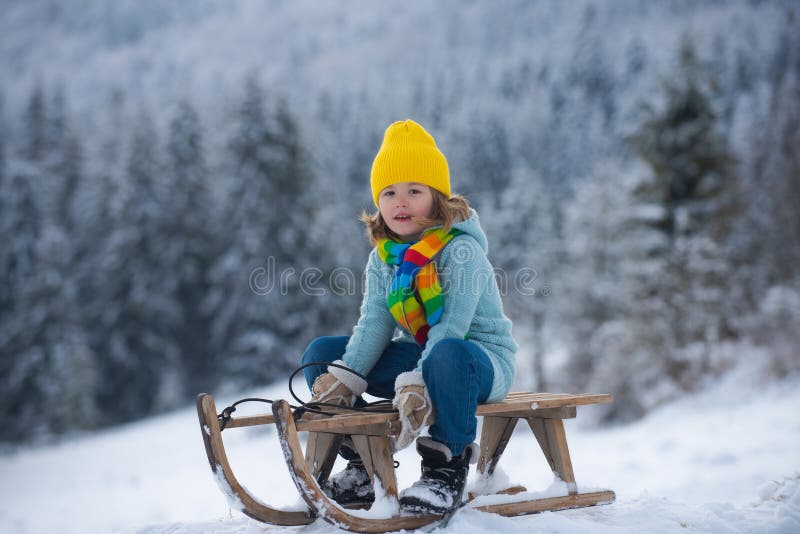 Boy sledding, enjoying sleigh ride. Child sitting on the sleigh. Children play with snow on winter background of snow