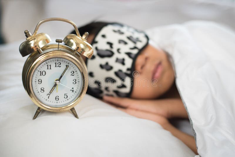 Boy sleeping on bed white piilow and sheets with alarm clork wearing sleep mask