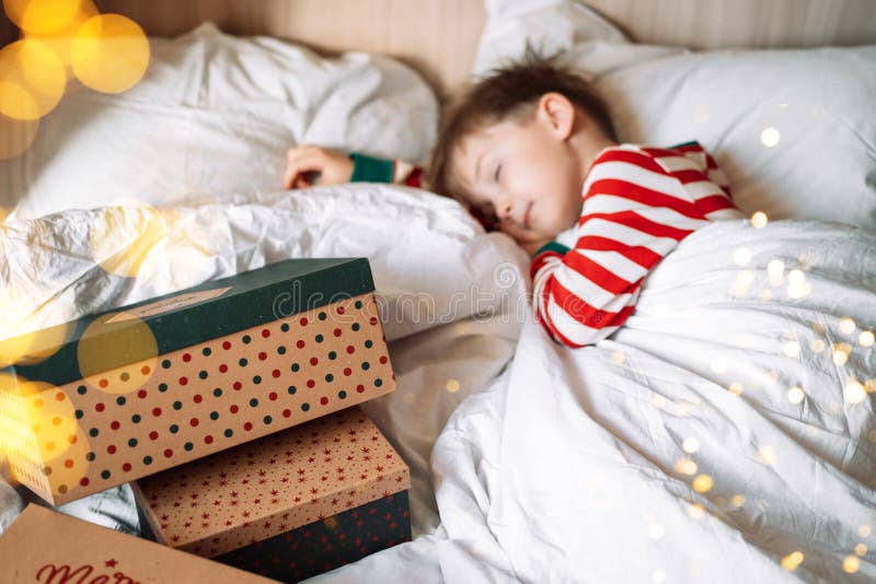 Boy Sleeping on White Bedding Next To Christmas Gifts Stock Image