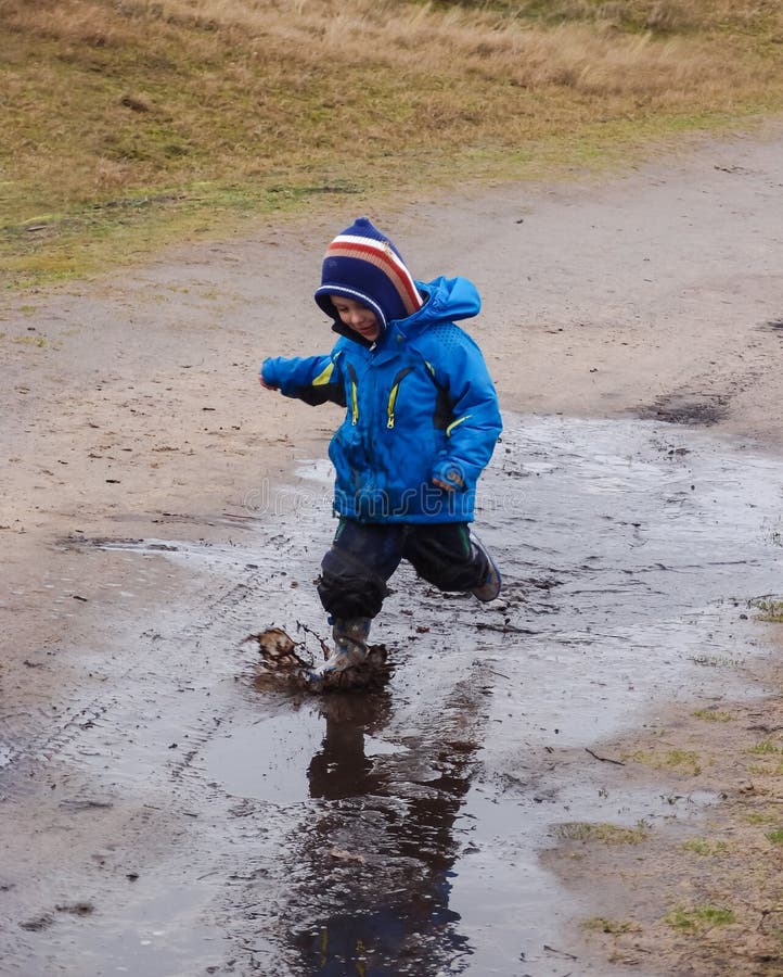 Small boy in winter clothing and rubber boots running through a muddy puddle in a winter dune landscape. Small boy in winter clothing and rubber boots running through a muddy puddle in a winter dune landscape