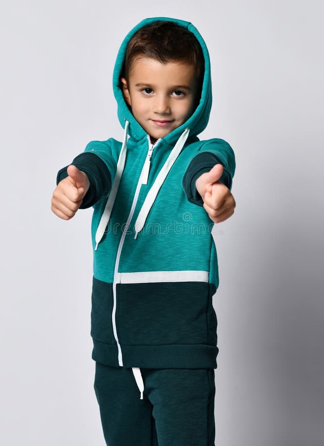 Boy in sportswear gesturing thumbs-up portrait. Boy in sportswear, showing thumbs up - cool. Little schoolboy in black green hooded tracksuit showing like sign stock images Boy in sportswear gesturing thumbs-up portrait. Boy in sportswear, showing thumbs up - cool. Little schoolboy in black green hooded tracksuit showing like sign stock images