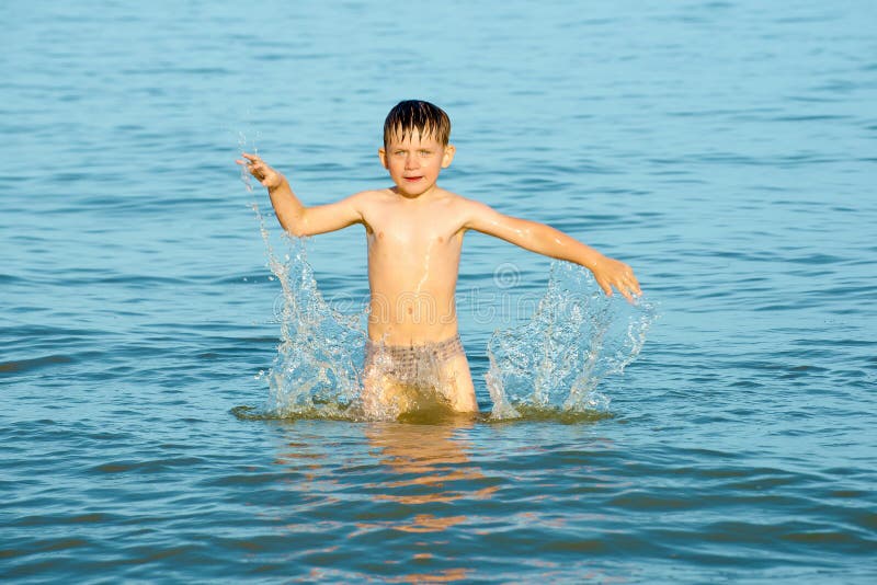 The boy sprinkles in the sea water on the ocean on a summer day and waving his arms in the direction of happiness and joy.