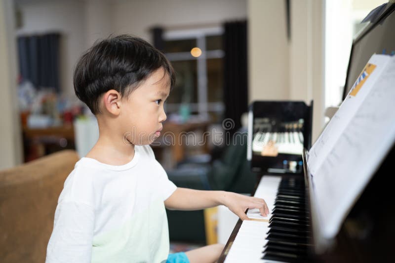 Foto de Young pianist boy looking at the digital tablet screen for learning piano  online at home. Music distance learning concept. do Stock