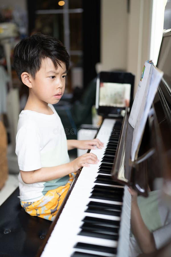 Foto de Young pianist boy looking at the digital tablet screen for learning piano  online at home. Music distance learning concept. do Stock