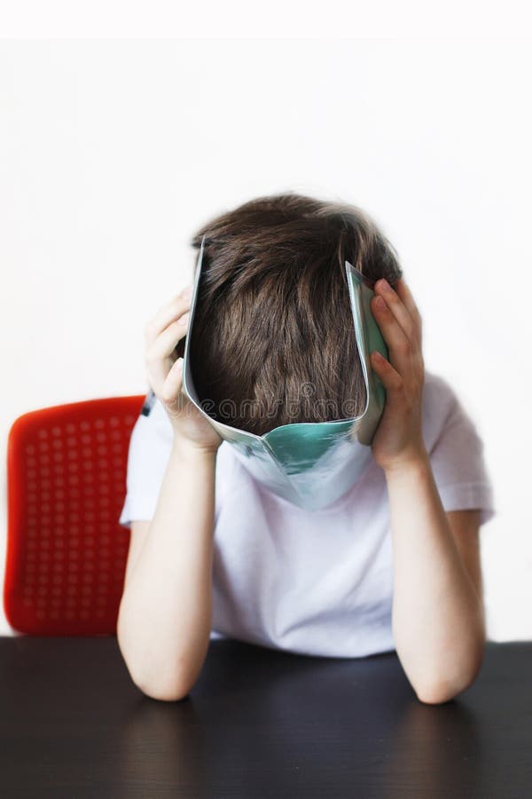 The boy is tired of doing homework. the child covered face with a notebook stock images.