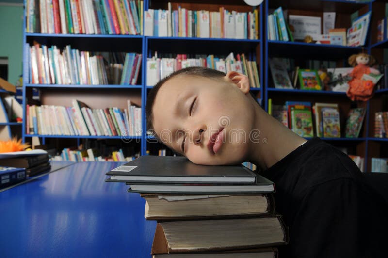 Boy tired sleeping on pile of books in library exausted of education