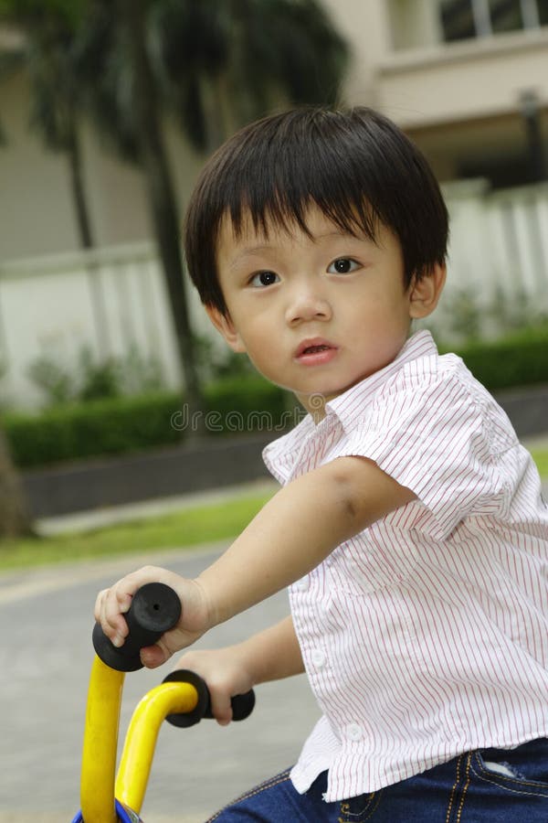 An Asian boy on a tricycle in a public park. An Asian boy on a tricycle in a public park