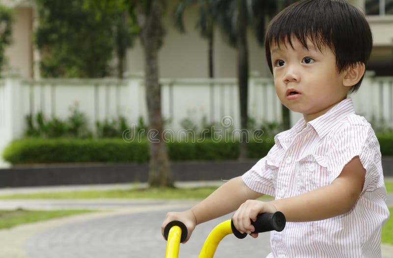 An Asian boy riding his tricycle in a public park. An Asian boy riding his tricycle in a public park