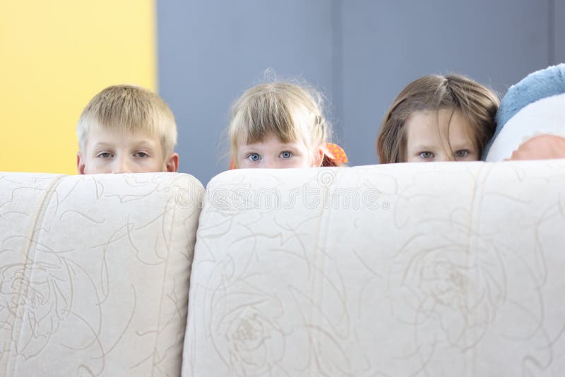 Hide And Seek On The Sofa Boy and Two Girls Hide Behind Sofa and Look Out. Stock Image - Image of